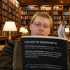 Person holding a book titled 'Log Out of Mediocrity' in a library setting